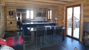 Interior de una cabaña de madera con cocina, comedor y chimenea.