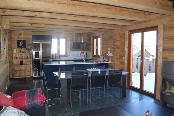 Interior de una cabaña de madera con cocina, comedor y chimenea.