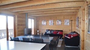 Interior de una cabaña de madera con una mesa de comedor, sillas, un sofá y un televisor.