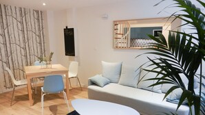 Una sala de estar moderna con un sofá, una mesa de comedor y sillas. Hay una pizarra en la pared y una ventana con persianas.