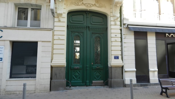 Un edificio con puerta doble verde, paredes blancas y un balcón con barandillas de metal decorativo.