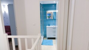 Pasillo que conduce a un baño con pared de azulejos azules, un lavamanos blanco y un tapete azul en el suelo.