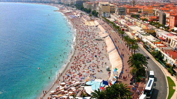 Un paisaje urbano costero con una playa concurrida, edificios a lo largo del paseo marítimo y una vista despejada del mar.