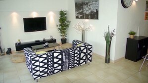 Una sala de estar moderna con un sofá estampado en blanco y negro, un televisor de pantalla plana en la pared, una planta en maceta y un accesorio de iluminación decorativo.