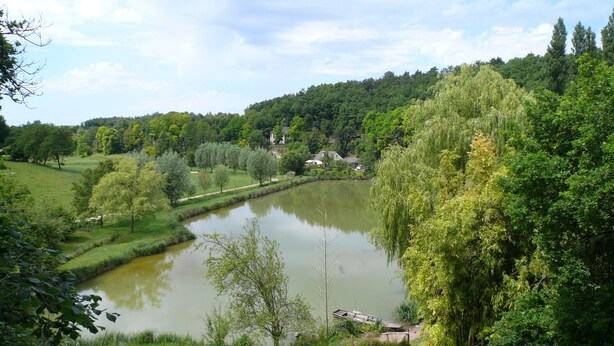 Eine friedliche Flusslandschaft mit einem kleinen Steg, üppigem Grün und einem Haus in der Ferne.