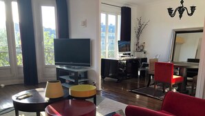 A modern living room with a flat-screen TV, a dining area with a table and chairs, and a view of the city through large windows. - like  a presidential suite with a magnificient view (Paris)