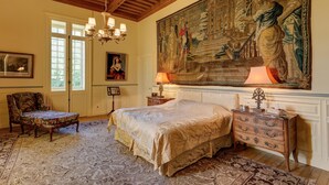 Un dormitorio con una cama grande, una silla, un aparador y un tapiz en la pared.