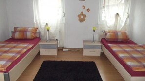 A room with two beds, each with a matching pillow and a bedside lamp. There is a black rug on the floor, and a wall decoration above the beds.