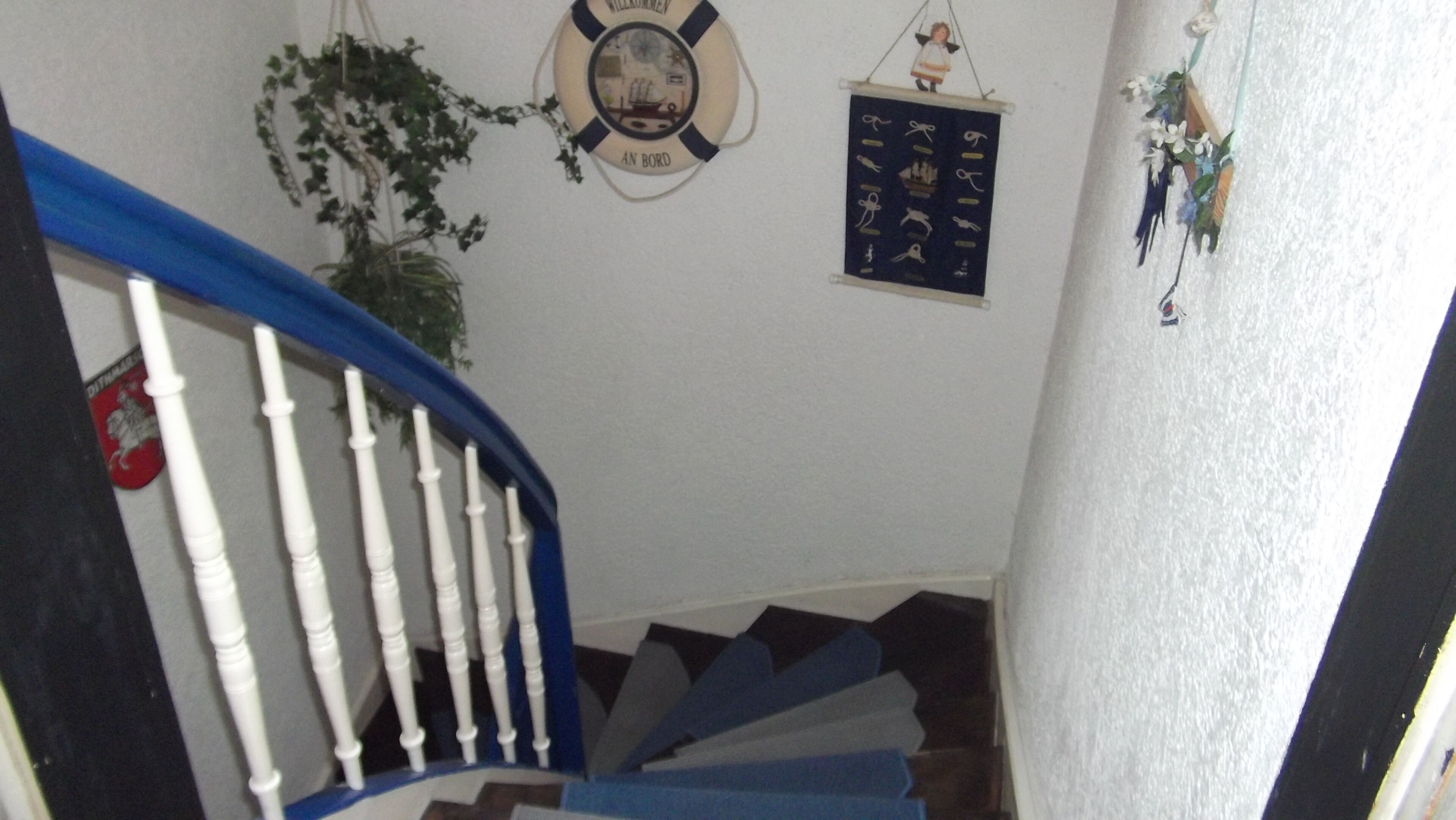 A staircase with white balusters and blue handrails, a life preserver with 'AN BORD' text, and a wall-mounted decorative item.
