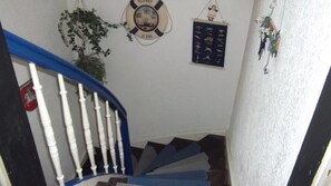 Un escalier avec des balustres blanches et des rampes bleues, une bouée de sauvetage portant l'inscription « À BORD », et un objet décoratif fixé au mur.