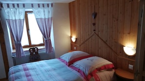 Een slaapkamer met een houten wandpaneel, een bed met beddengoed met een patroon, een raam met gordijnen en wandlampen.