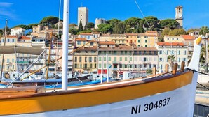 A boat with the number NI 304837 docked near a harbor with colorful buildings and a tower in the background. - CANNES low  California LUXURY T2 65M2, SWIMMING POOL, PARKING NEAR CROISETT (Cannes)