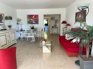 Una sala de estar con un sofá rojo, una mesa de comedor con sillas, una mesa de centro y una planta en maceta.