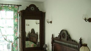 A bedroom with a wooden bed, floral curtains, a mirror, and a clock on the wall. - Charming 70m2 villa with private pool (Castelnau D'auzan Labarrère)