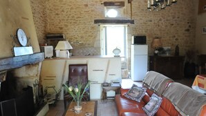 Ein rustikales Interieur mit einer Steinwand, einer Holzbalkendecke, einem Kamin, einem Ledersofa und einer Küchenzeile mit Fenster.