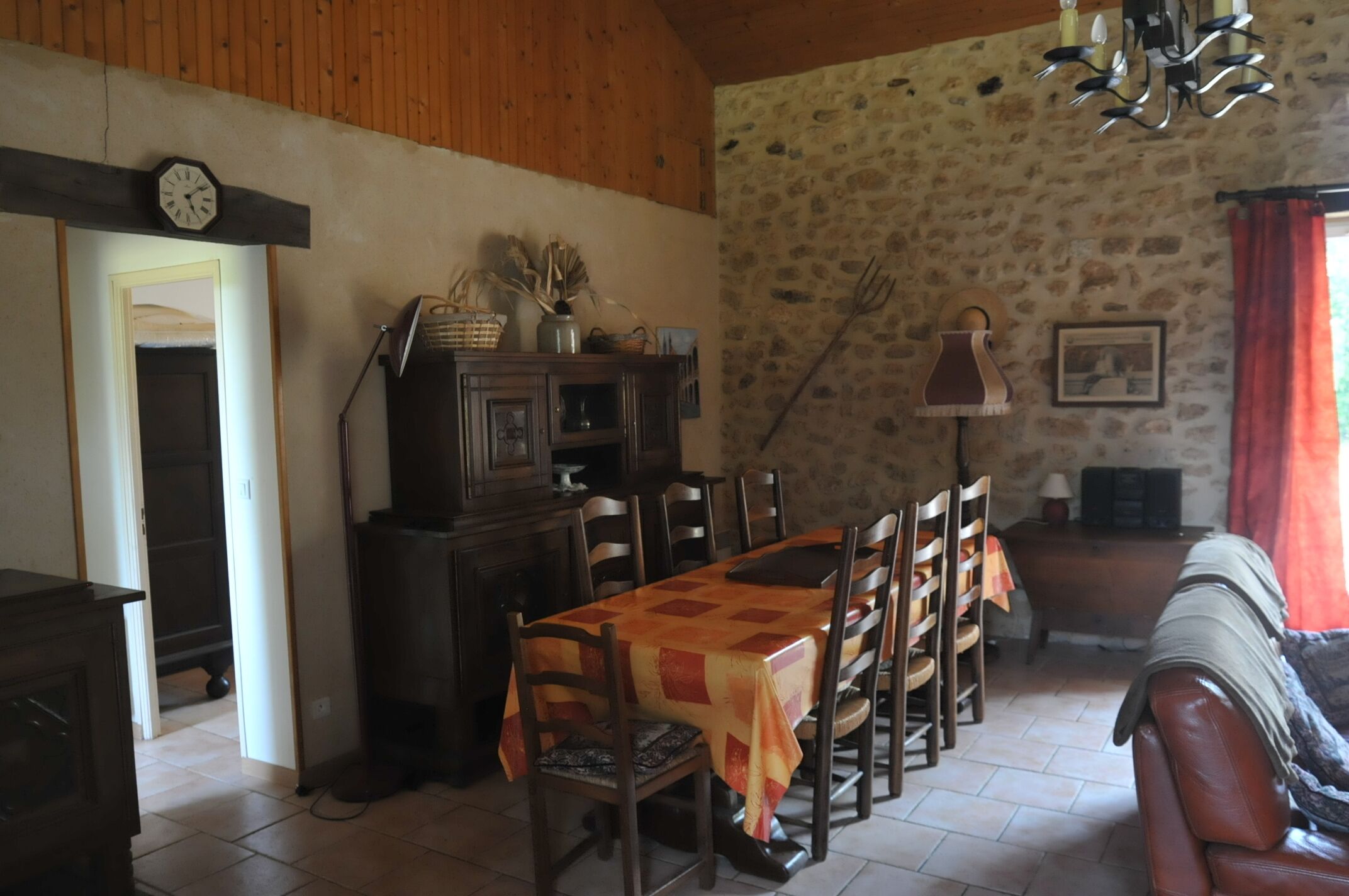 Comedor con mesa y sillas de madera, pared de piedra y una lámpara de araña.