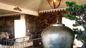 Un jarrón metálico grande sobre una mesa de madera en una habitación con paredes de piedra y una escalera.