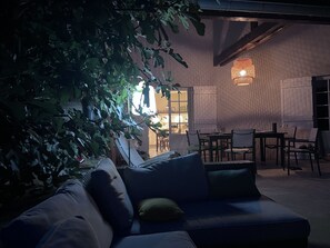 Et hyggeligt udendørs opholdsområde med en mørkeblå sofa og hynder, omgivet af frodigt grønt løv.