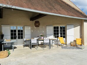 En udendørs patio med et spisebord, omgivet af stole og en gul lænestol.