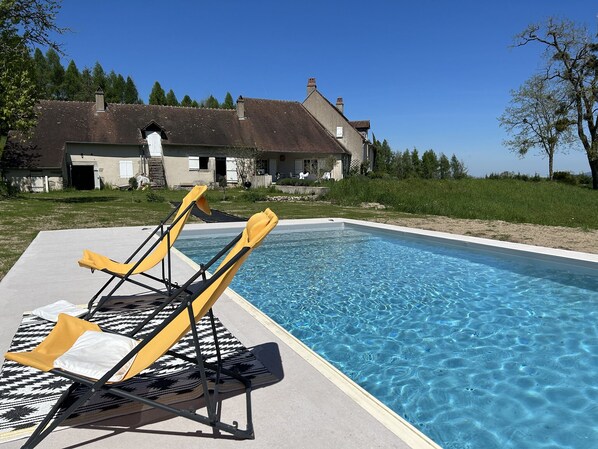 En swimmingpool med liggestole og et hus i baggrunden.