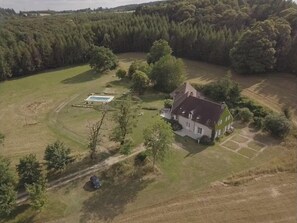 Oversigtsbillede af en ejendom med et stort hus, en swimmingpool og grøn bevoksning omkring.