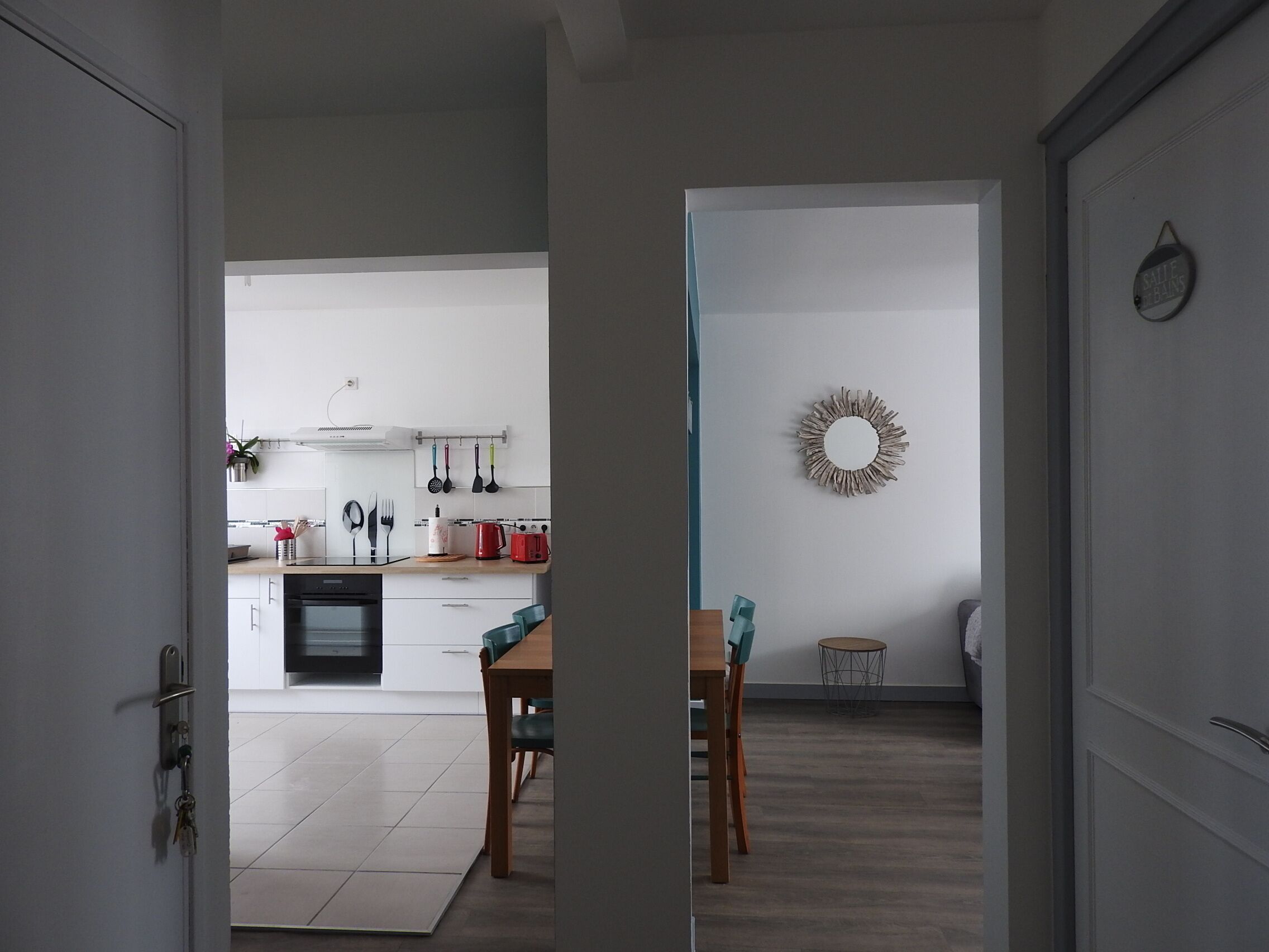 Een moderne keuken met witte kasten, een eethoek met een houten tafel en stoelen, en een decoratieve spiegel.