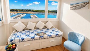 Una cama con vista a un puerto deportivo, una silla azul y un frutero sobre una mesa.