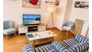 Una sala de estar con televisión, sofá, sillones, una mesa de centro y una lámpara.