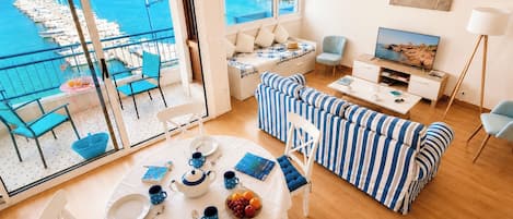 Un vaste espace de vie avec un balcon donnant sur une marina, un canapé, une table à manger et un téléviseur.