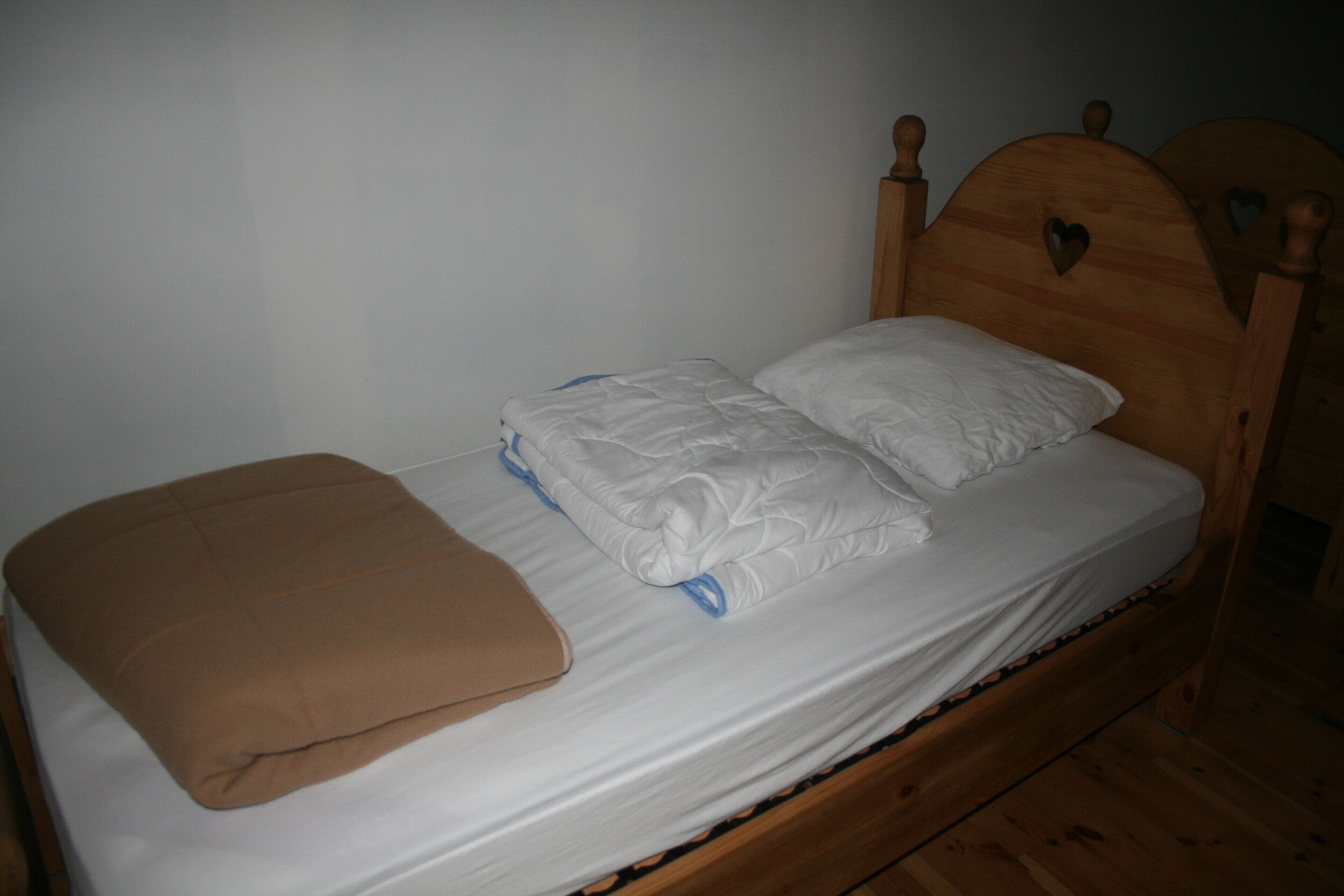 A single bed with a wooden headboard, a brown blanket, and two pillows.