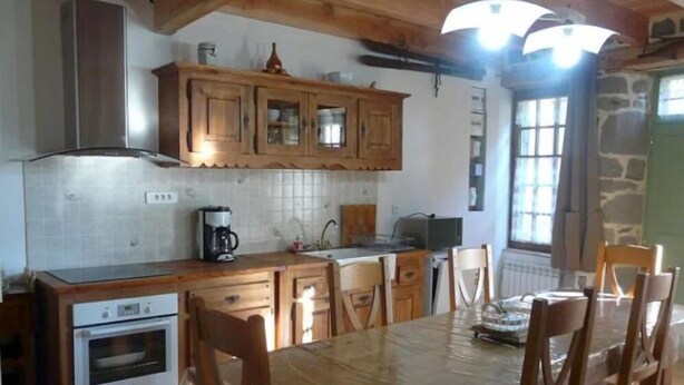 Una cocina con armarios de madera, salpicadero de azulejos, cafetera y una mesa de comedor con sillas.
