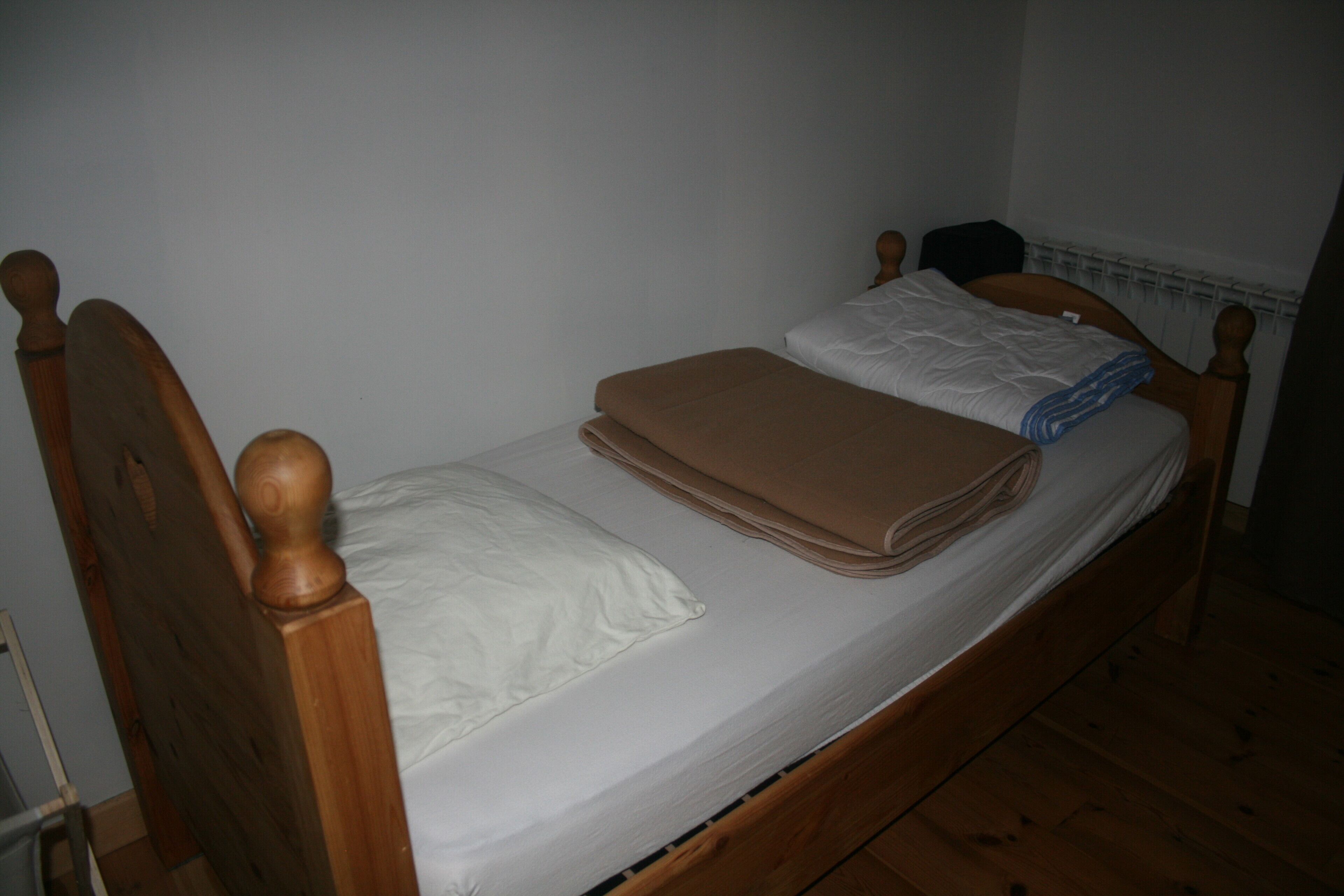 A single bed with a wooden headboard and footboard, white bedding, and a brown blanket.