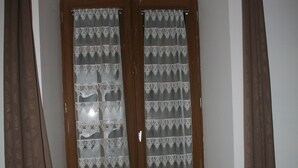 Una habitación con techo de madera, una ventana con cortinas estampadas, cama de madera y suelo de madera.