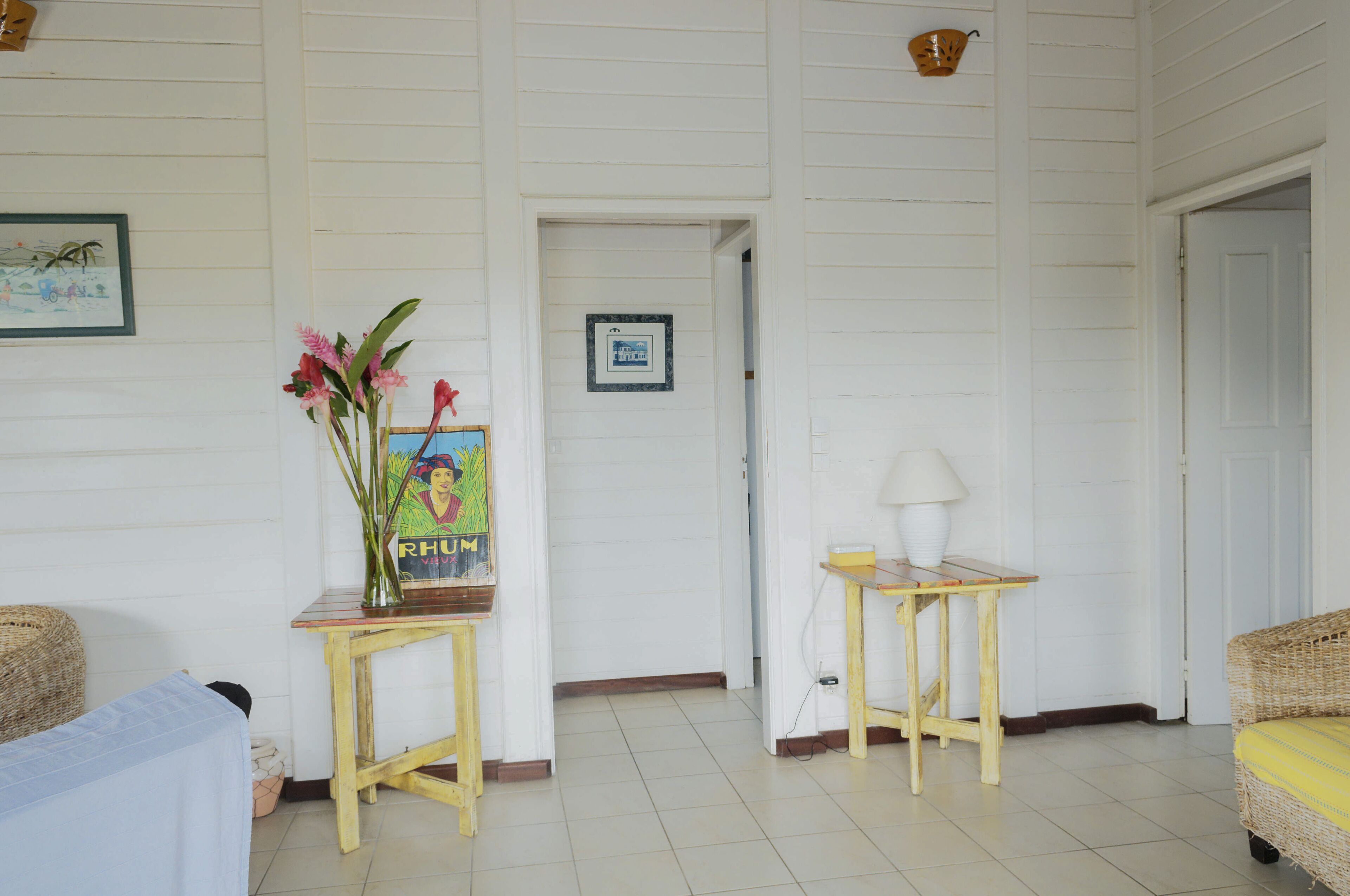 A room with a bed, a small table with a lamp, a wicker chair, and a painting on the wall.