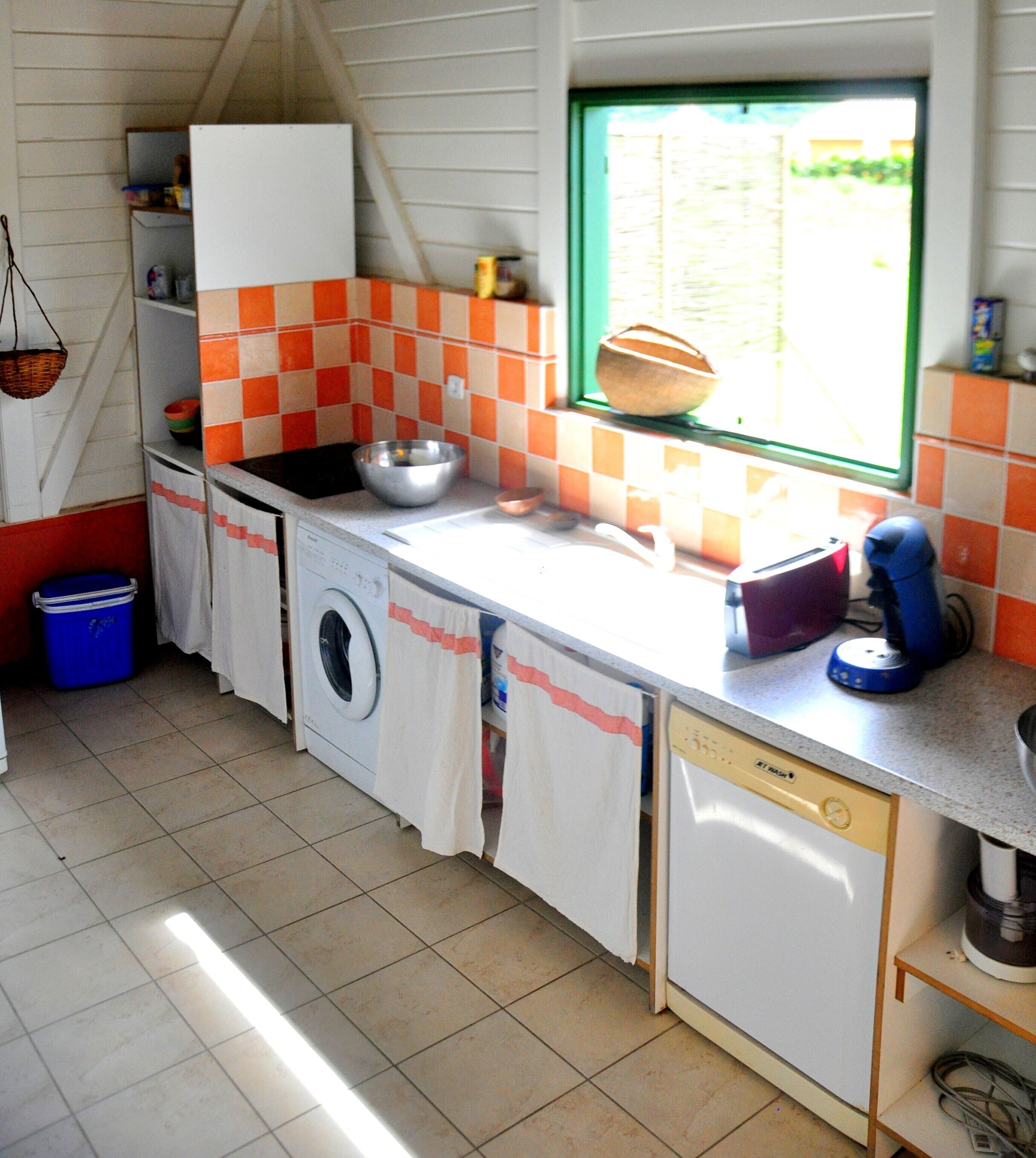 Een kleine keuken met een wasmachine, een vaatwasser en een raam met uitzicht op groen.