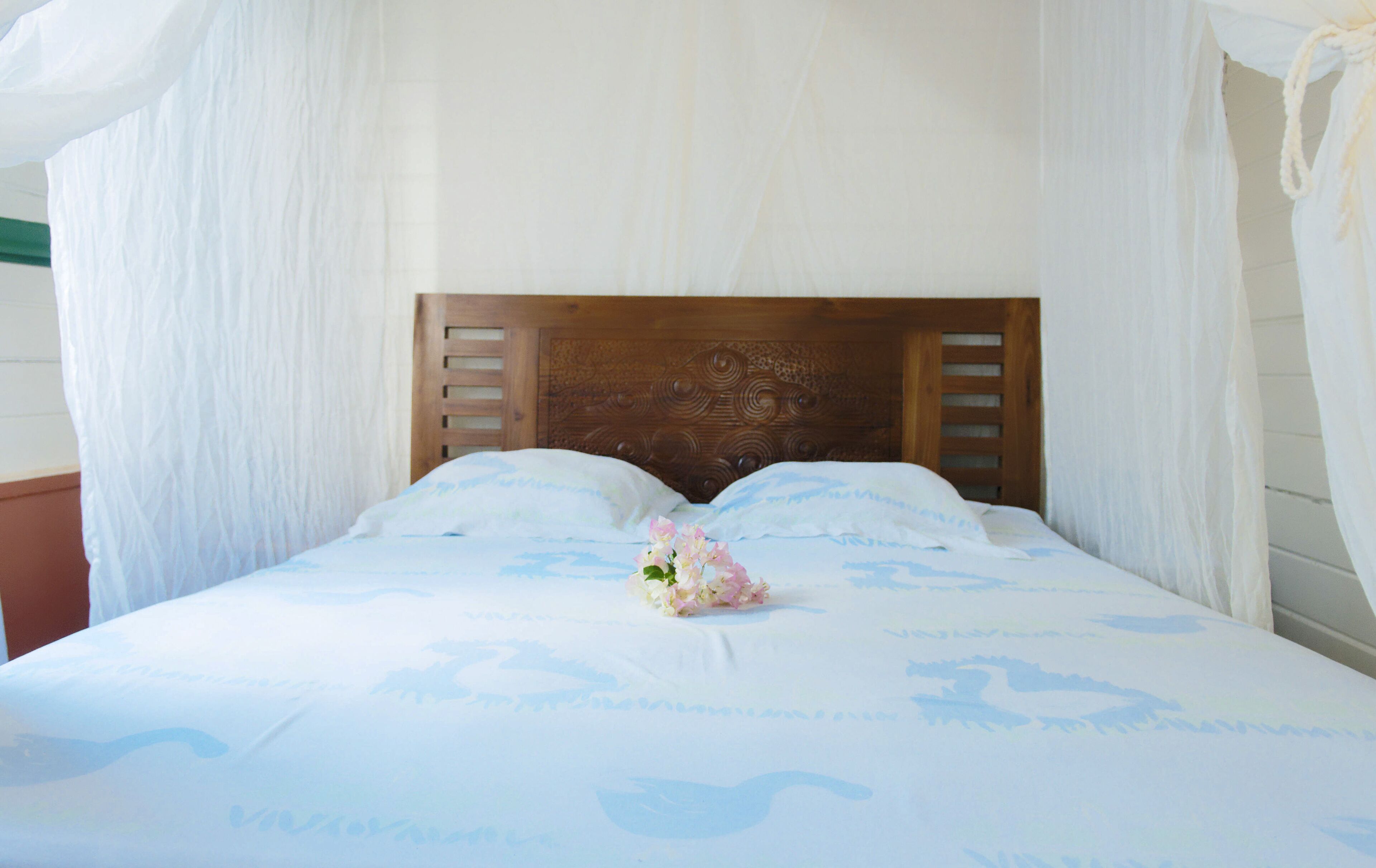 A bed with a wooden headboard, white bedding, and a floral arrangement.
