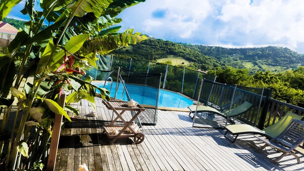 Una terraza de madera con sillones de descanso y una piscina, rodeada de vegetación exuberante y un paisaje montañoso.