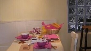 Ein Esstisch gedeckt mit rosa Geschirr und einem Brotkorb, im Hintergrund ein Fenster.