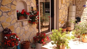 Ein Gebäude aus Stein mit einer Pflasterterrasse, Topfpflanzen und einem Wassertank.