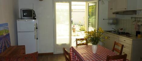 Cocina compacta con zona de comedor, un televisor sobre un refrigerador blanco y una ventana con vista a vegetación.