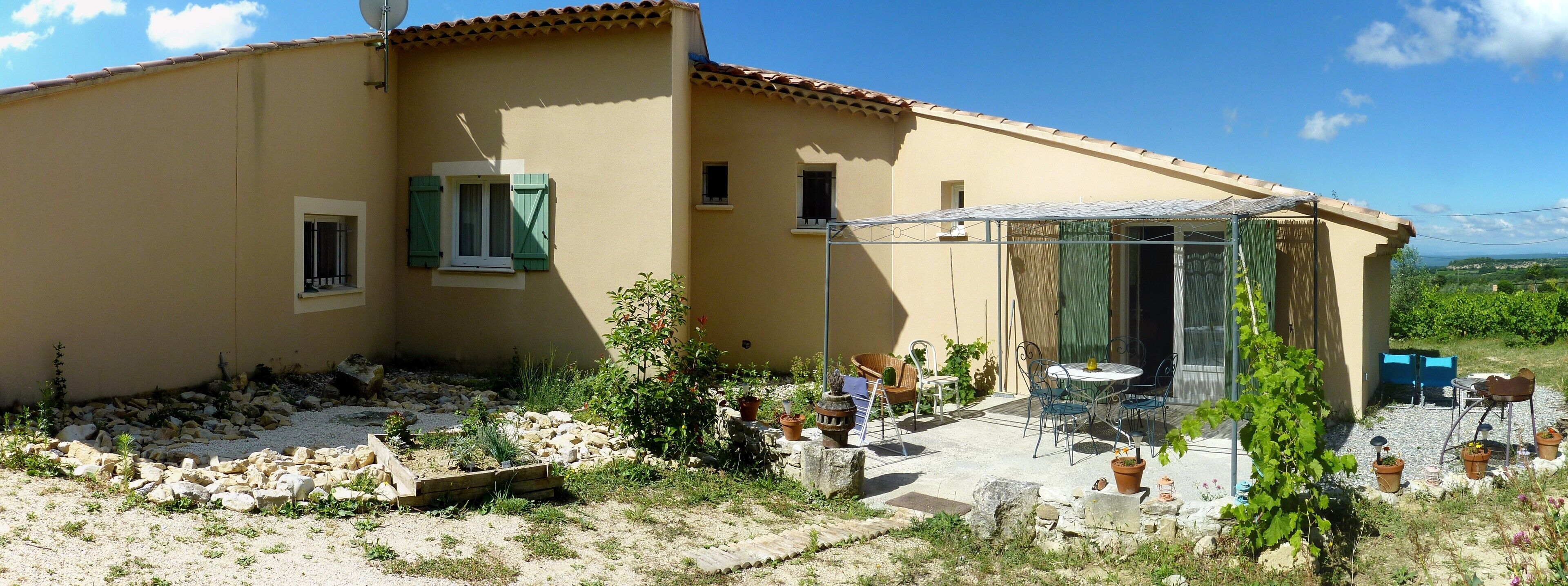A house with a patio area, a small garden, and a table with chairs.