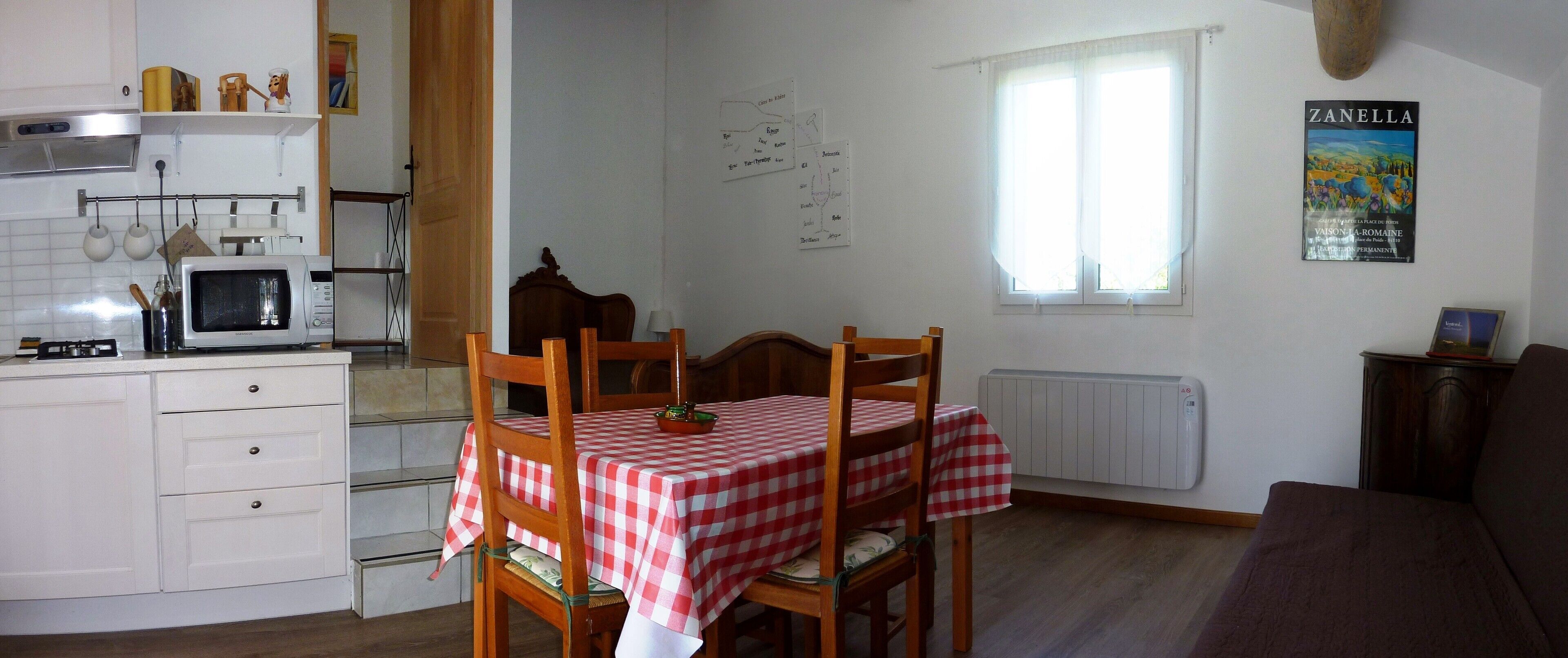Eine kleine Küche mit Mikrowelle, einem Holztisch mit kariertem Tischläufer und einem Fenster mit Blick auf die Landschaft.