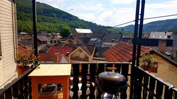 Een balkon met een houten tafel en een barbecue, met uitzicht op een stad met rode daken en groene heuvels.