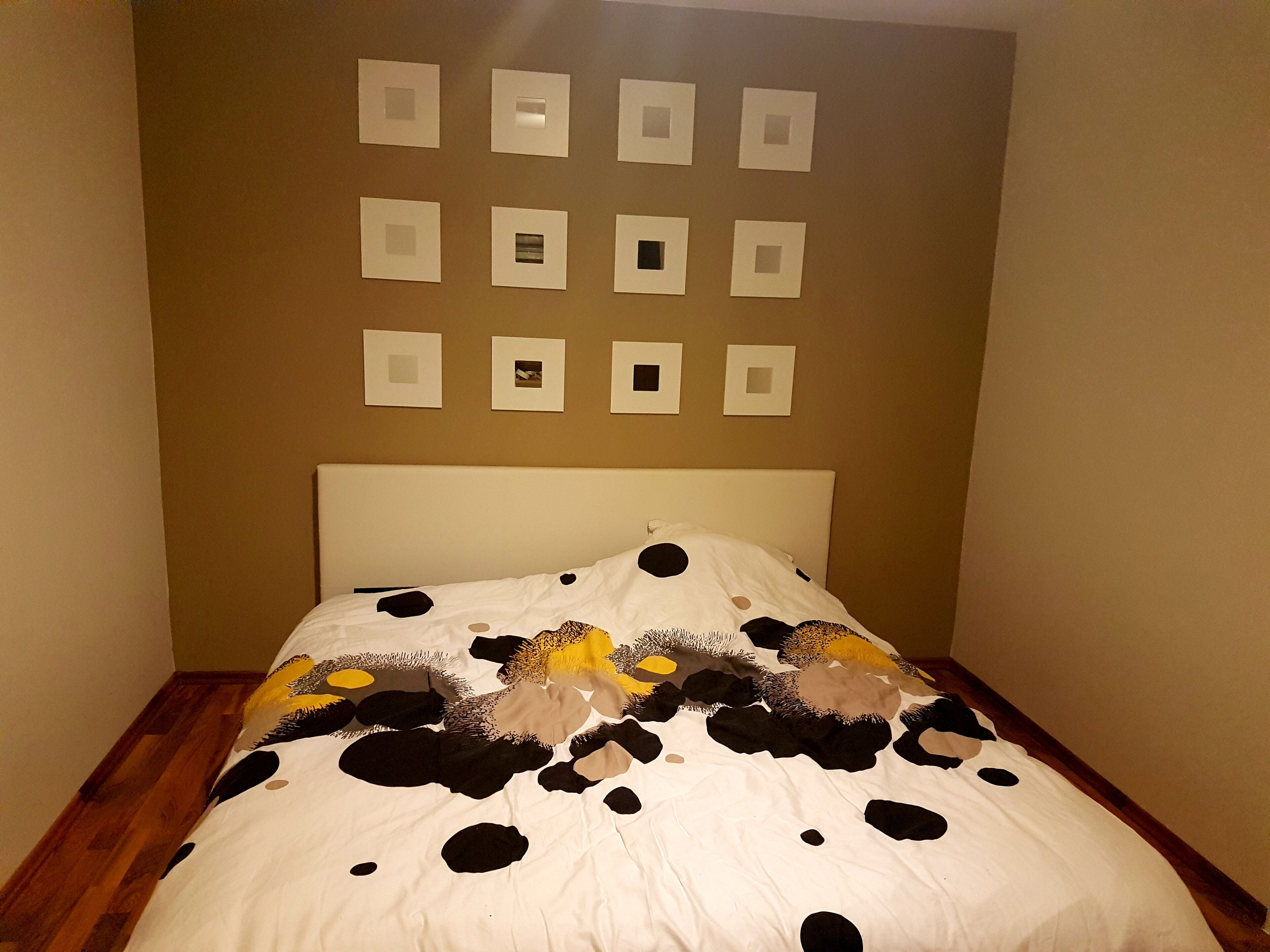A bedroom with a bed, a headboard, and a wall with framed pictures.