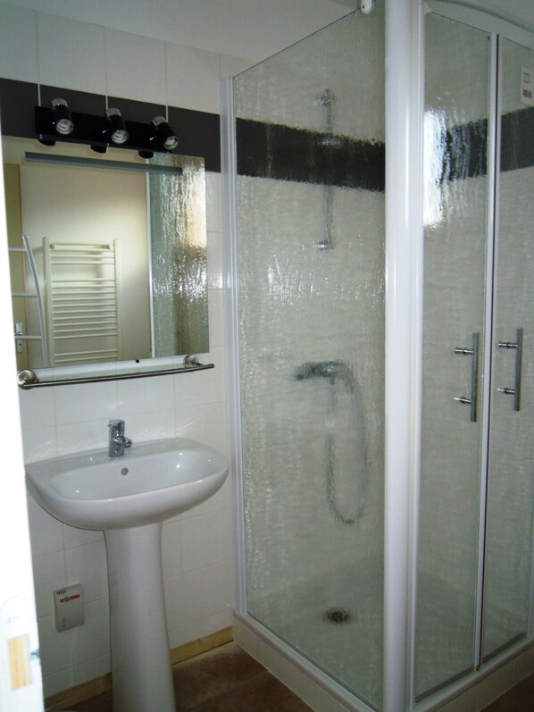 Une salle de bain avec une douche à parois de verre, un lavabo sur colonne et un miroir au-dessus du lavabo.