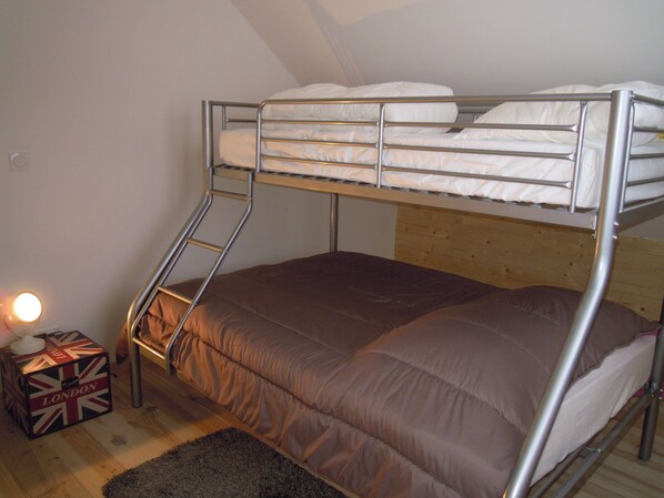 Un lit superposé avec une tête de lit en bois, un matelas marron et une échelle en métal. On peut voir une petite boîte décorée d’un motif Union Jack sur le sol.