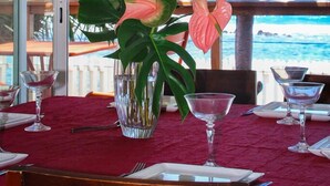 A dining table with a red tablecloth, clear glassware, and a tropical plant arrangement. - Waterfront villa with swimming pool. Exceptional view (saline les bains)