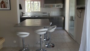 Una cocina moderna con una isla central, taburetes de bar, una ventana con vistas y una puerta corredera de cristal.