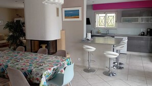 Una cocina moderna con una isla grande, taburetes de bar y un comedor con mantel colorido.