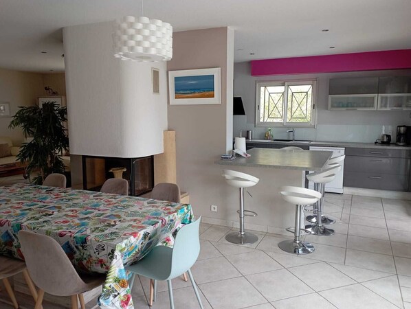 A modern kitchen with a large island, bar stools, and a dining area with a colorful tablecloth.
